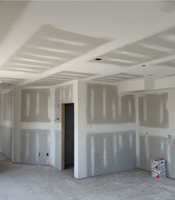 Open room with a fully taped ceiling grid and joint compound drying on the walls